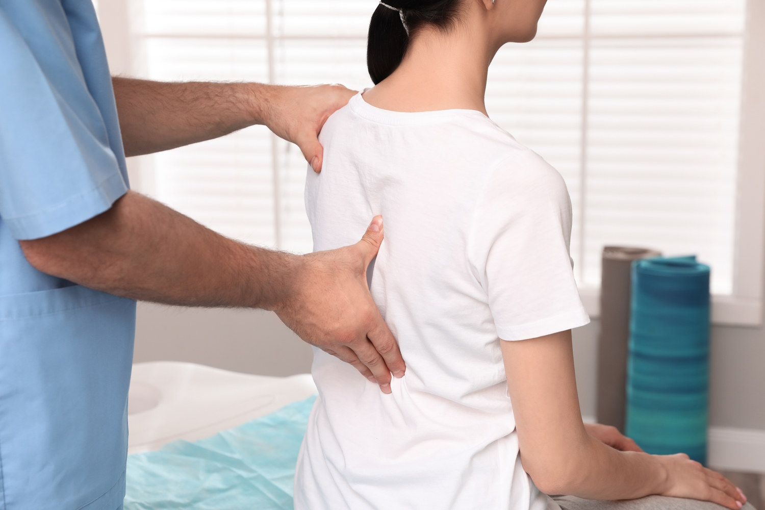 Ein Orthopäde untersucht den Rücken einer Patientin. Die Patientin sitzt vor ihm auf einer Liege.